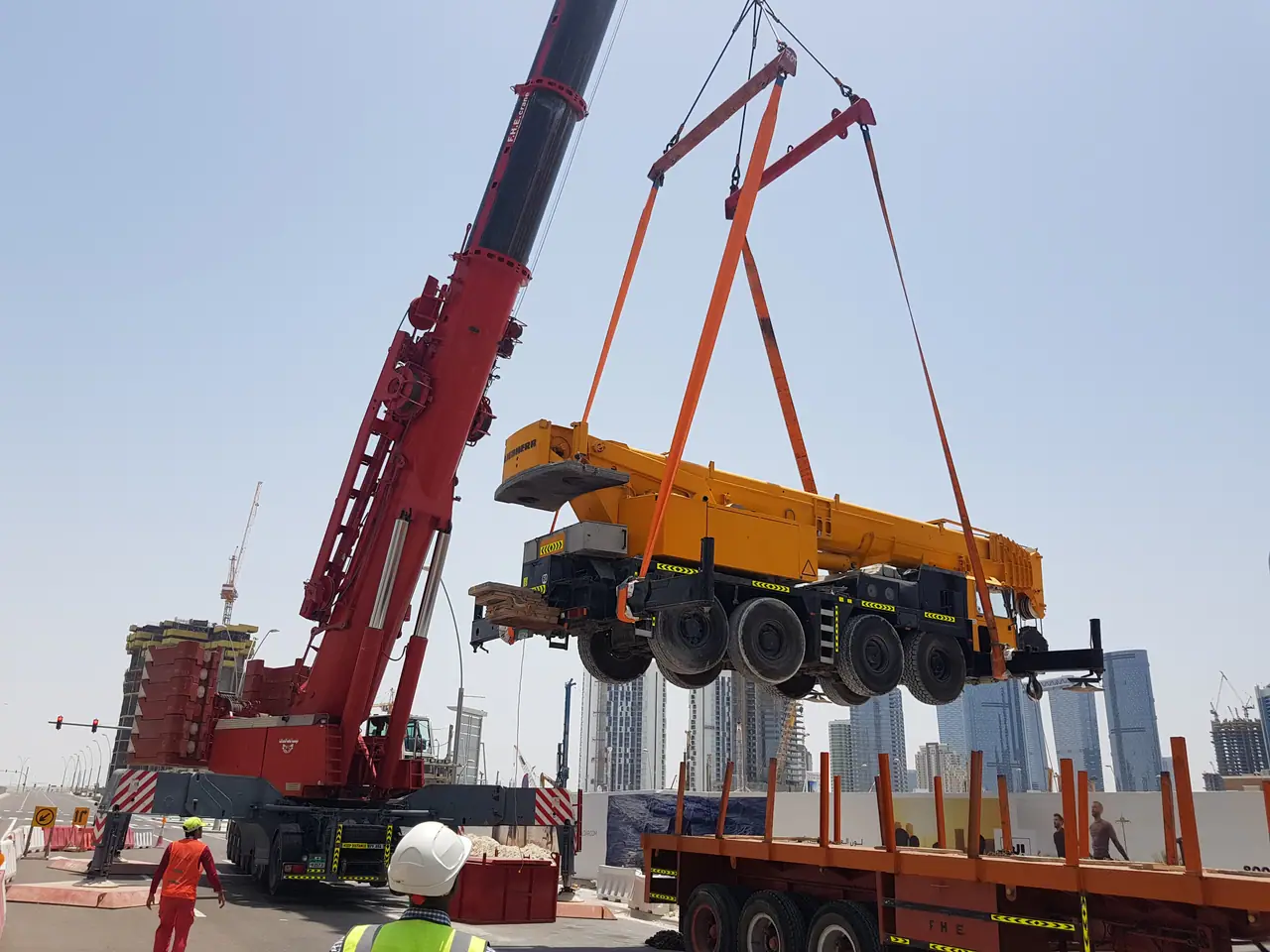 Heavy crane lifting a mobile crane carrier onto a flatbed trailer with orange round slings