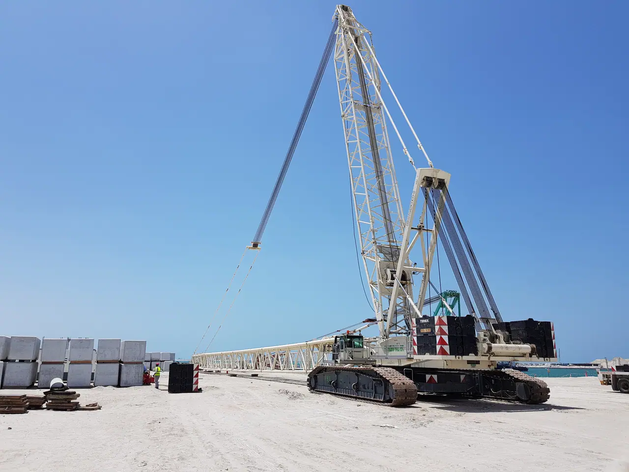 White lattice-boom crawler crane working on a coastal site
