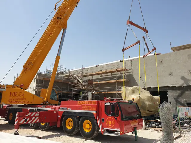 FHE-branded all-terrain crane lifting wrapped plant equipment into a building
