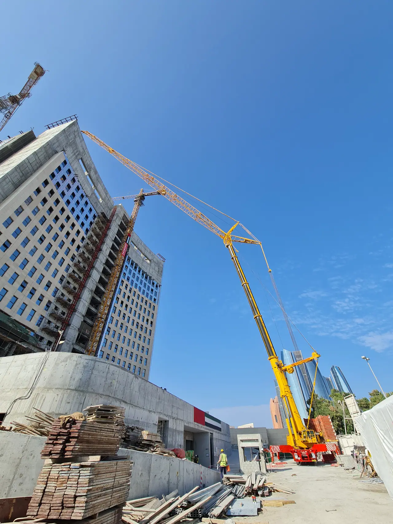 Yellow luffing crane reaching up a high-rise facade