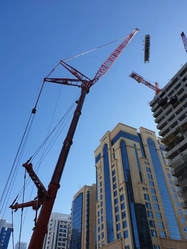 Red lattice luffing crane rising between high-rise towers