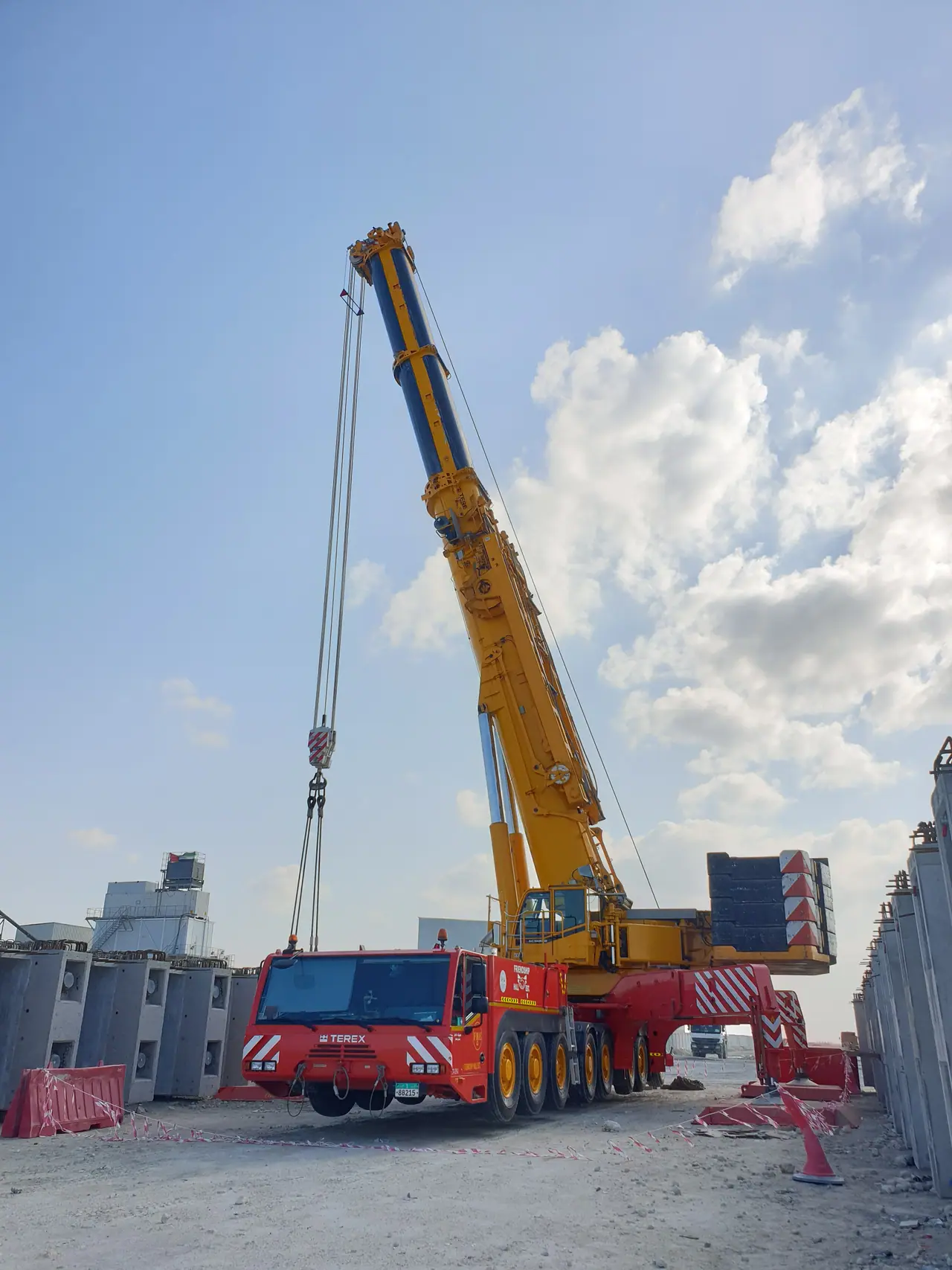 Red and yellow all-terrain crane rigged under a cloud-streaked sky
