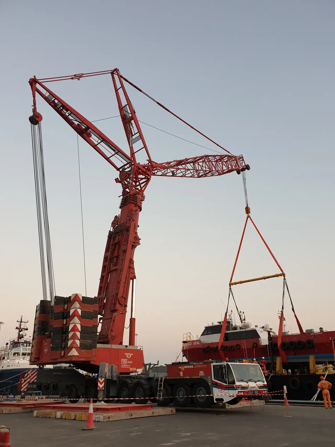 Red luffing-jib crane lifting a vessel at a port at dusk