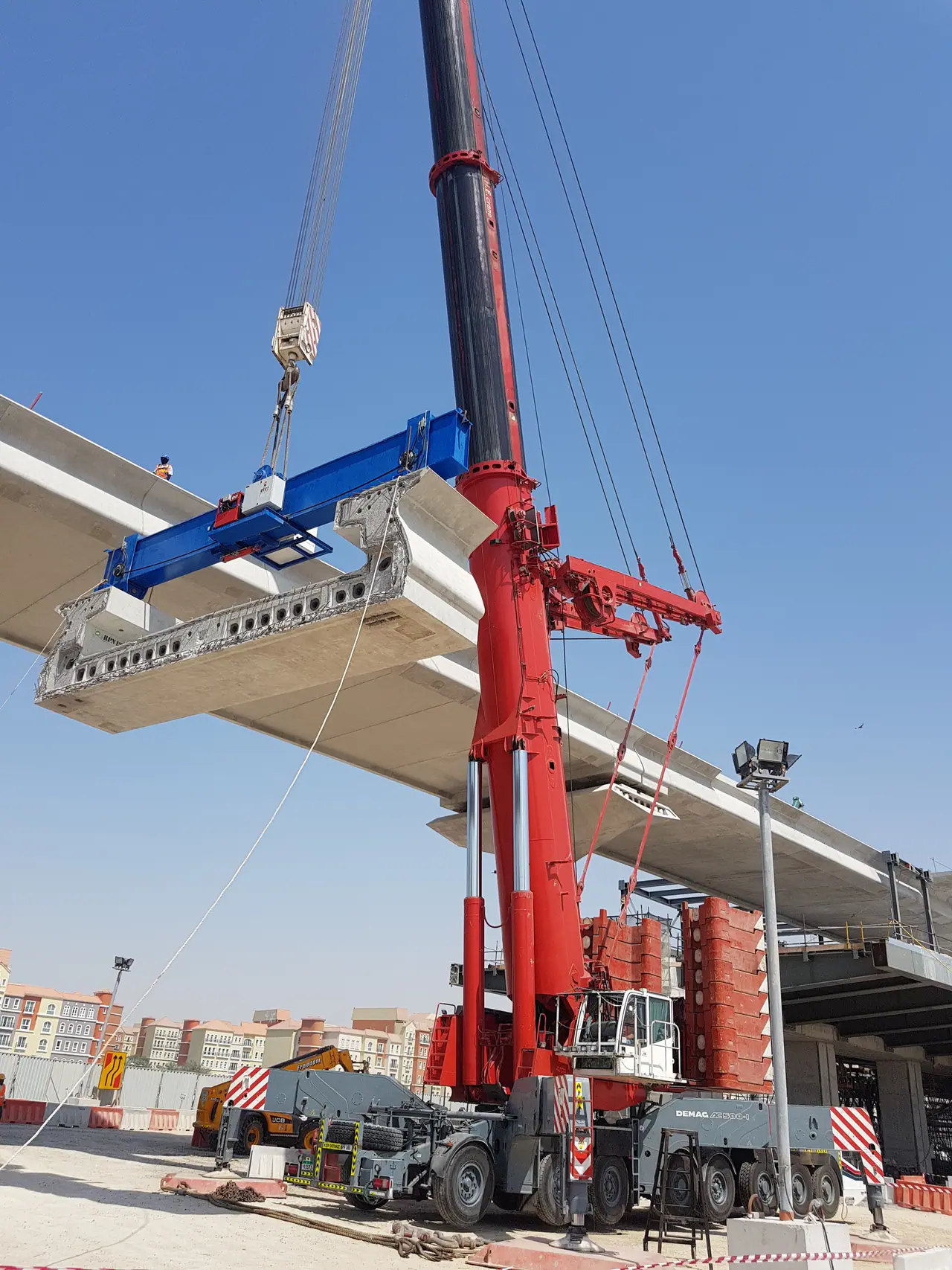 Red heavy crane setting a precast bridge segment using a blue spreader beam