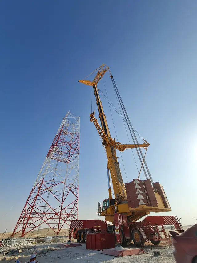 Heavy crane rigged between two red-and-white lattice transmission towers