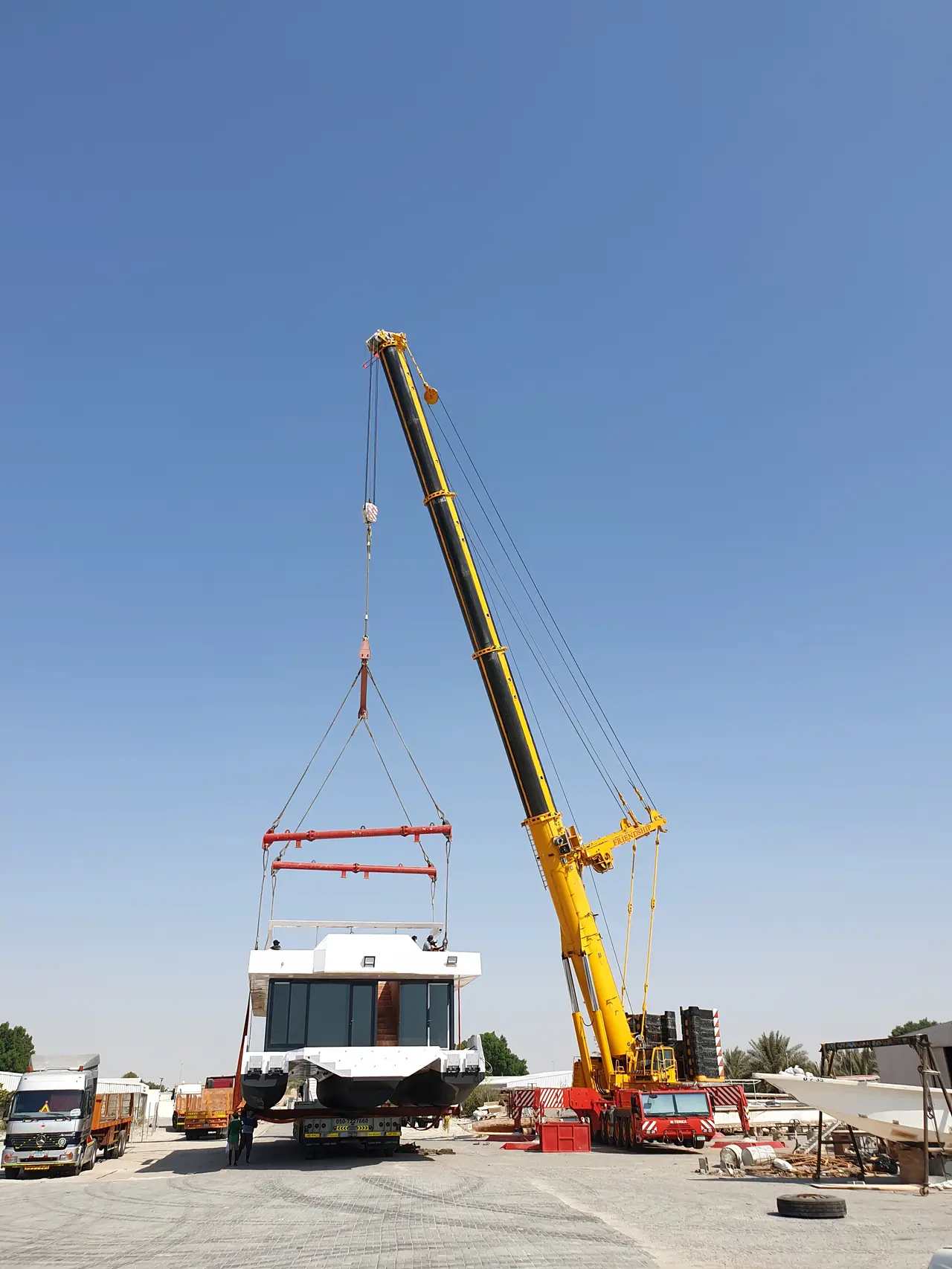Yellow mobile crane lifting a yacht hull with a spreader frame